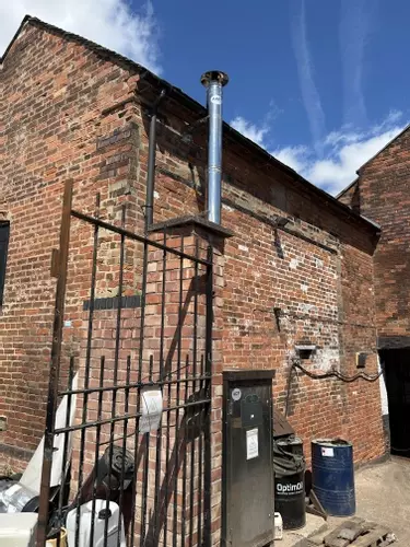Nilfisk DTE static pressure washer fitted with a stainless steel flue extension at a brewery in Burton, installed to safely redirect boiler exhaust fumes away from a confined courtyard cleaning area.